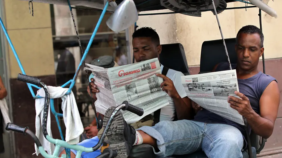 Dos bicitaxistas leen el diario oficial Granma y Juventud Rebelde.