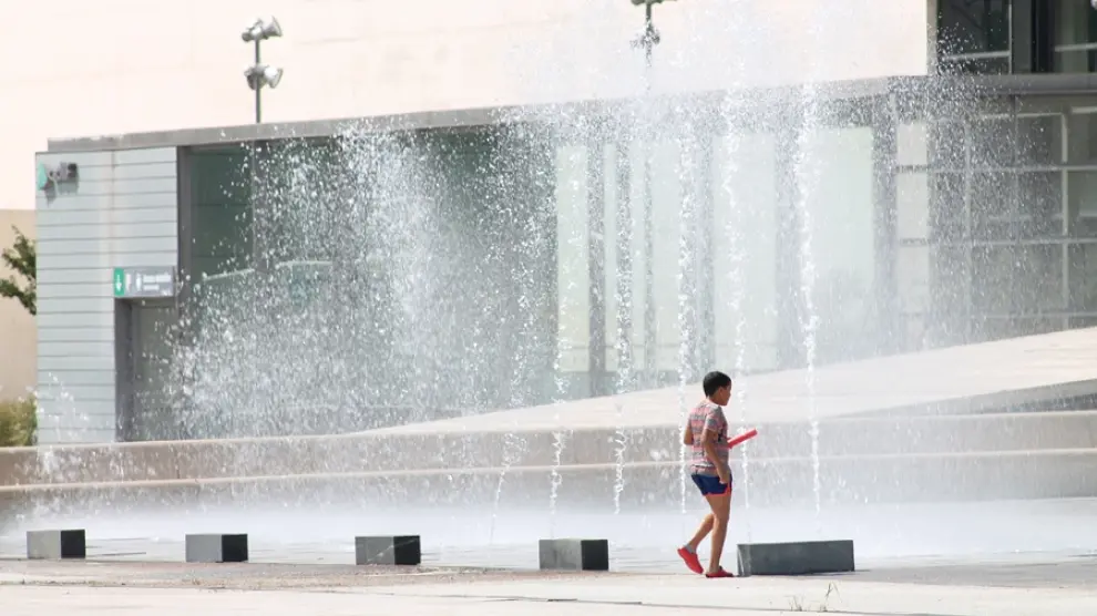 Un joven se refresca en una fuente de Zaragoza.