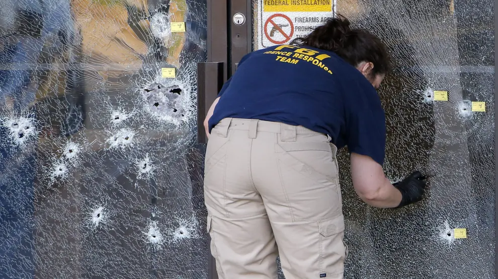 Una agente del FBI inspecciona un cristal lleno de disparos