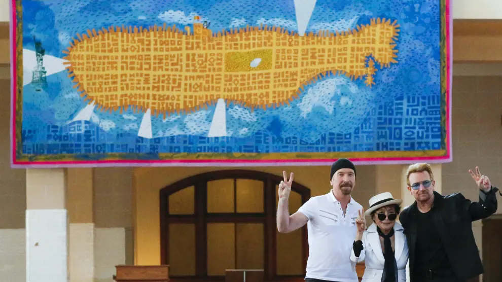 Yoko Ono, Bono y The Edge posan junto al tapiz.