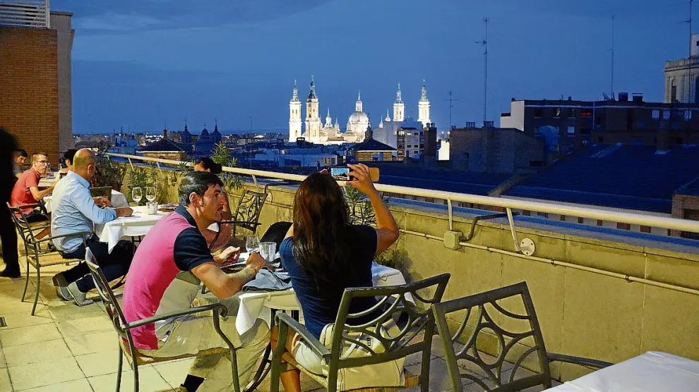 Varios clientes disfrutan de las vistas desde la terraza, con la basílica del Pilar al fondo.