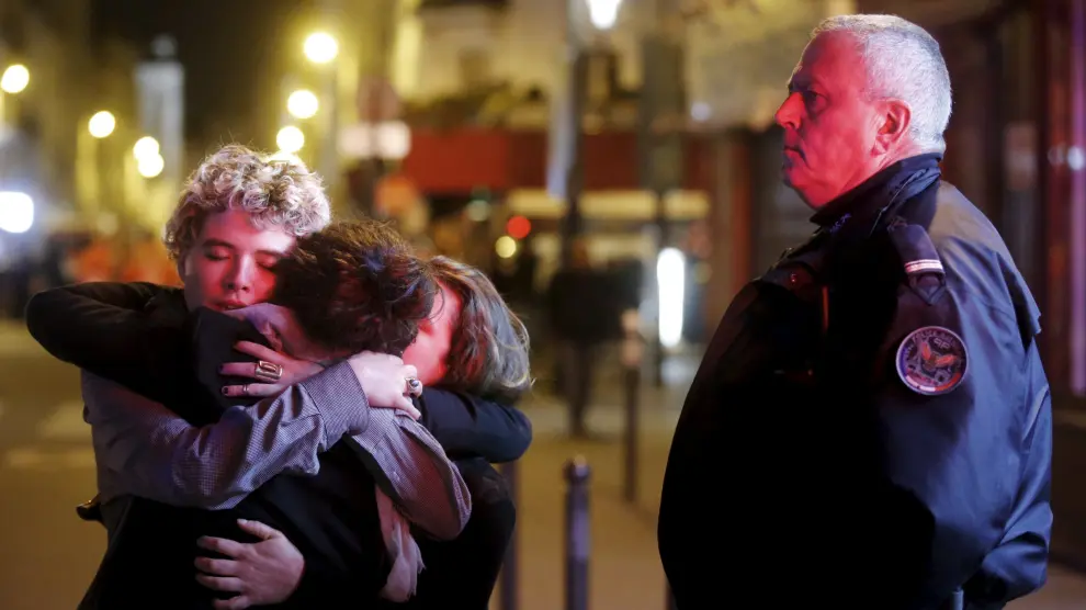 Tres personas se abrazan ante la mirada de un Policía