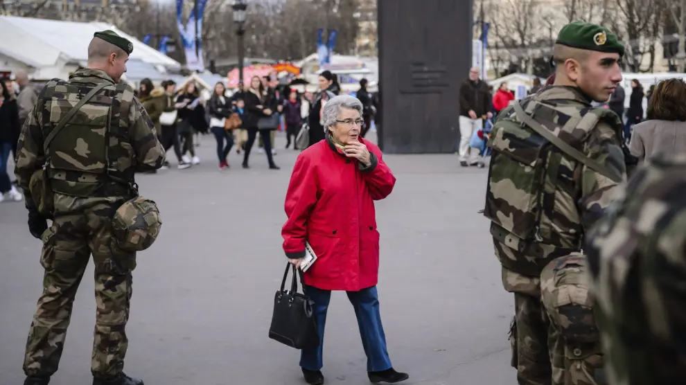 Una mujer camina junto a dos soldados franceses.