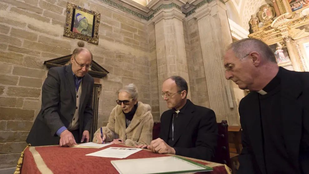 Teresa Ramón, junto al obispo de Huesca, Julián Ruiz,(sentado), firma la entrega de la obra de Santa Catalina de Alejandría que cuelga detrás, en la catedral de Huesca,