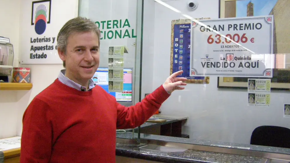 El administrador de lotería Ángel Marqueta señala el cartel que anuncia el premio.
