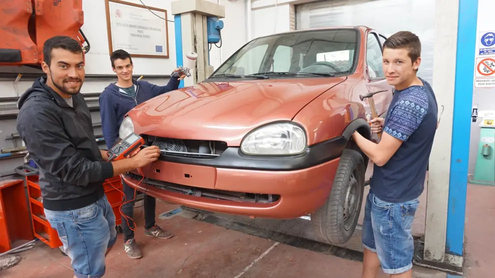 En la foto, los tres alumnos de automoción del IES Martínez Vargas arreglando un coche en el taller del centro.