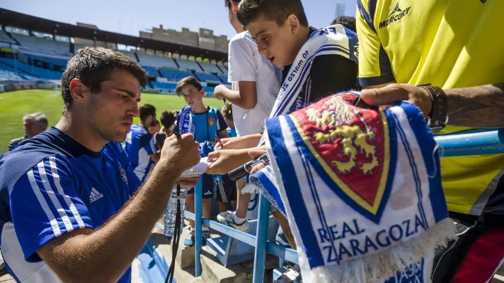 Alberto Zapater firma autógrafos a unos jóvenes aficionados zaragocistas, ayer en el estadio de La Romareda.