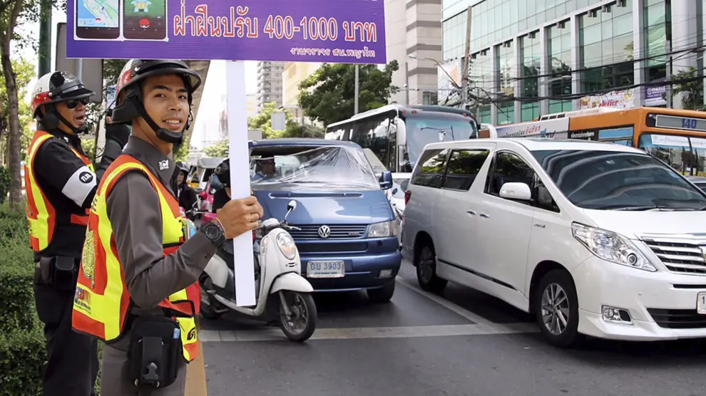 Un agente sostiene un cartel en el que se recuerda que está multado jugar mientras se conduce.