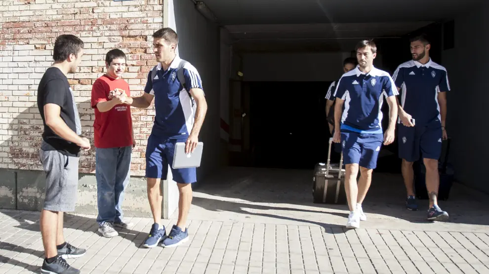 Zapater saluda a unos aficionados antes de la salida del Real Zaragoza rumbo a Sevilla este viernes. Del aparcamiento del club salen Lanzarote y Ratón junto a otros compañeros.