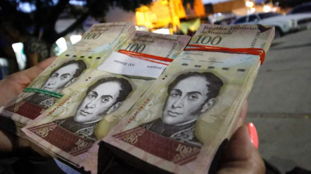 Una mujer sostiene varios billetes de 100 bolívares para cambiarlos.