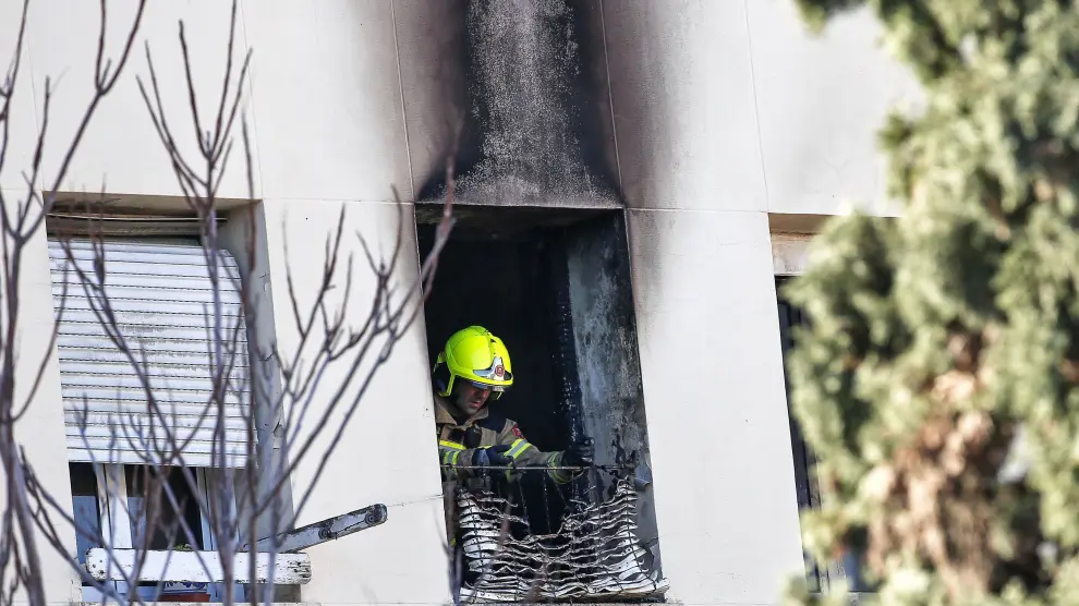 Un bombero retira una persiana quemada de la vivienda en la que este mediodía se ha declarado un incendio, en el que ha fallecido una mujer de 64 años al precipitarse desde un tercer piso.
