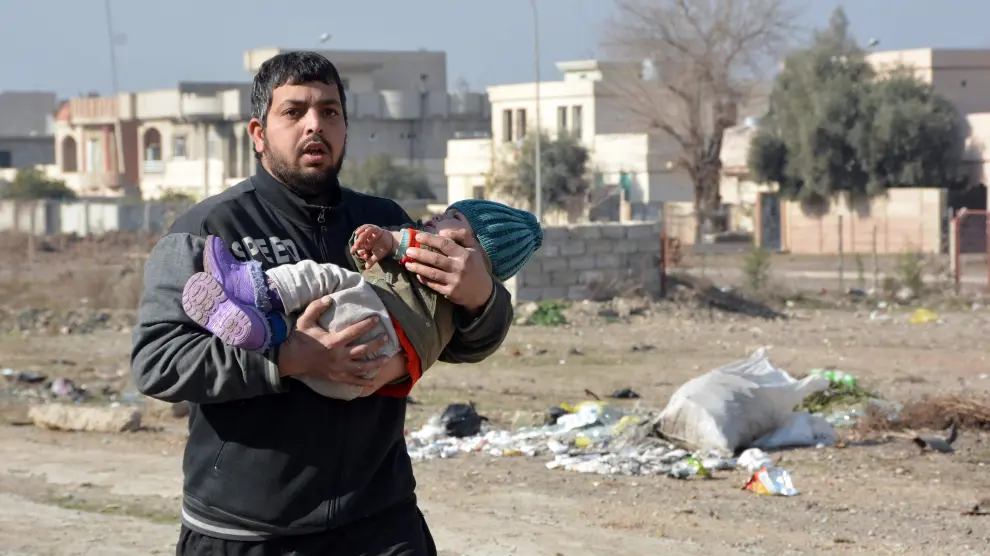 Un hombre corre con un niño en brazos huyendo de los bombardeos en Mosul, este viernes.