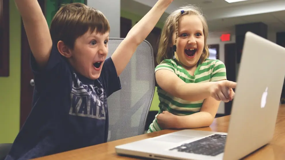 Dos niños jugando a un vídeojuego en un ordenador portátil.