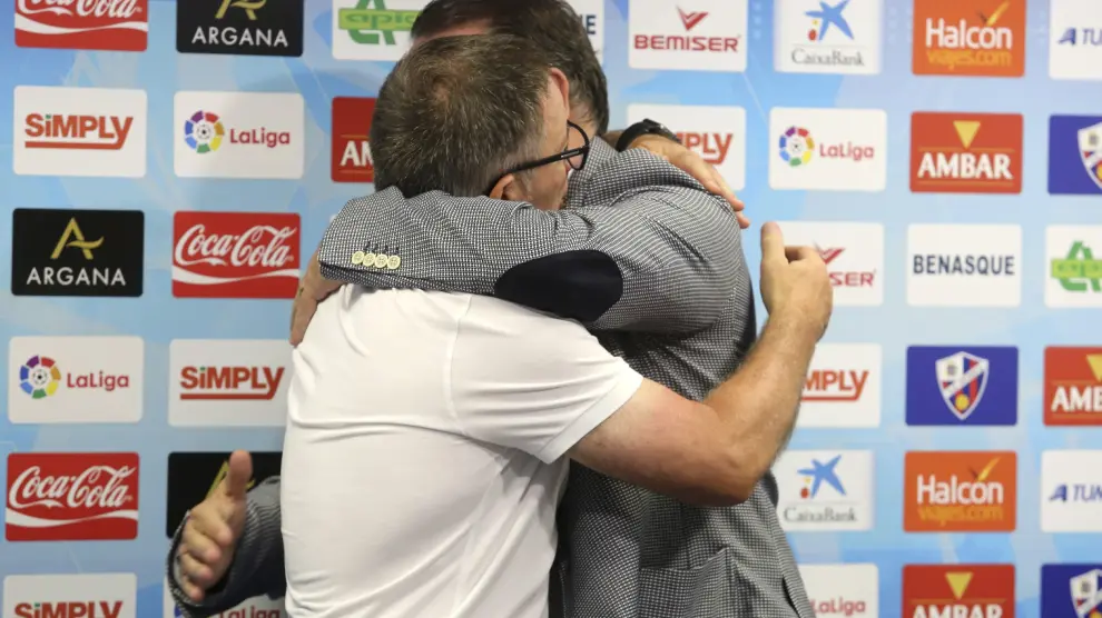 Juan Antonio Anquela, de blanco, se abraza con el presidente de la SD Huesca, Agustín Lasasosa.