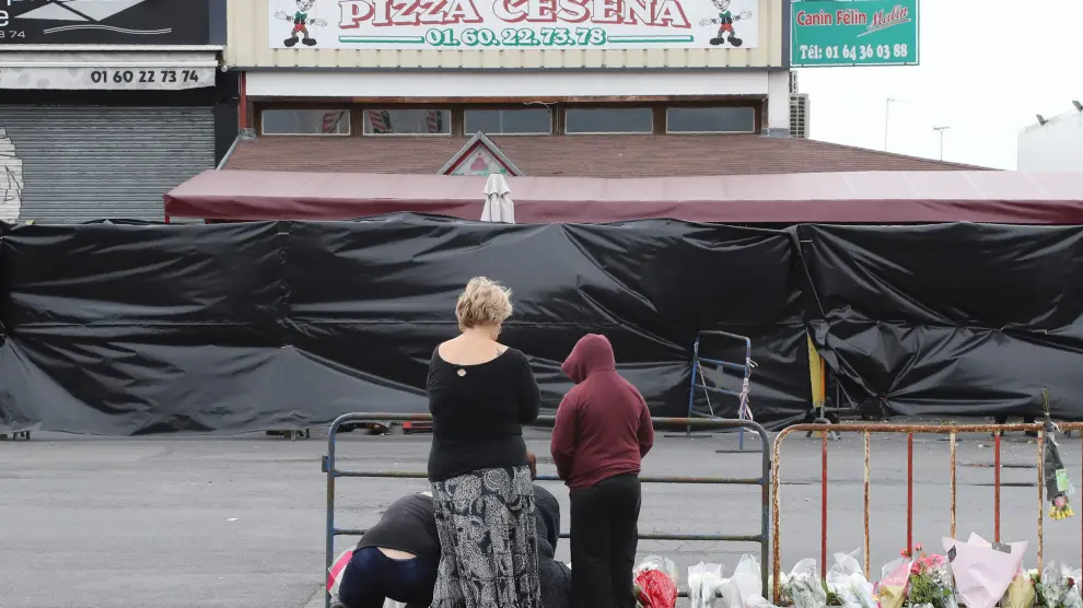Varias personas depositan flores frente a la pizzería donde ocurrió el atropello mortal.