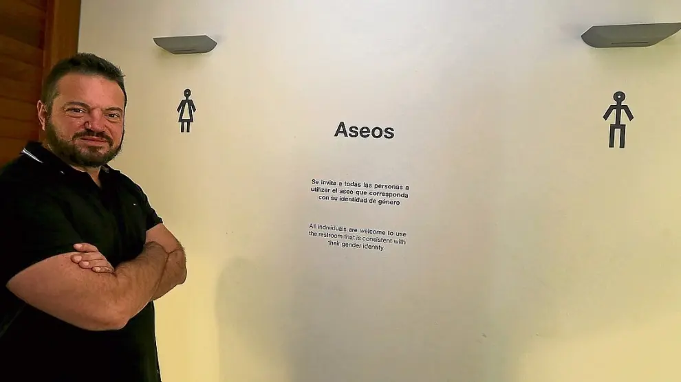 Juan Guardiola junto al cartel que invita a "utilizar el aseo que corresponda con su identidad de género".