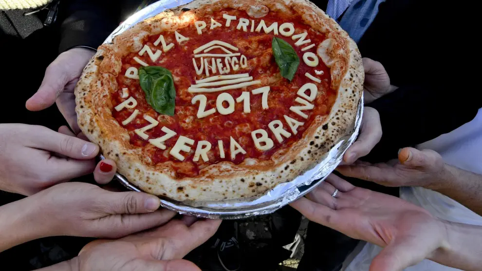 Varias personas sostienen una pizza en la plaza del Plebiscito en Nápoles.