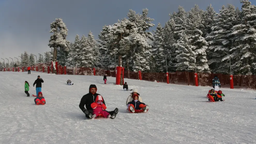 Niños y mayores juegan con la nieve en la zona acotada para trineos.