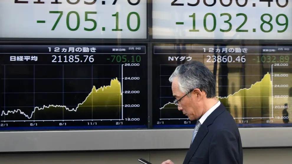 Un peatón camina delante de unos paneles que muestran los indicadores financieros de la Bolsa de Tokio