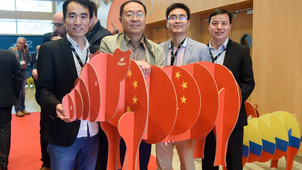 Imagen de cuatro clientes chinos que asistieron al último Encuentro Técnico Internacional que organiza Magapor anualmente en Zaragoza, sostienendo la figura de un cerdo elaborado por la entidad con la bandera su país.