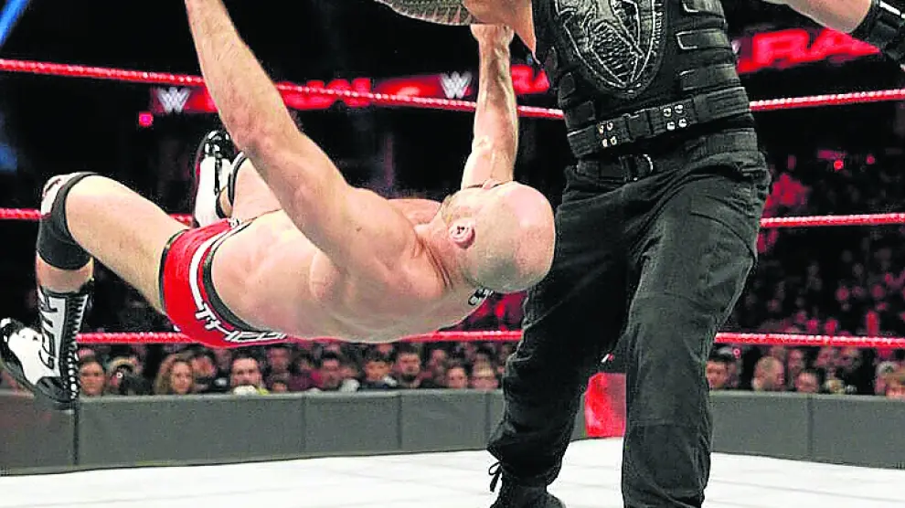 El luchador Roman Reigns empuja a un rival sobre la lona.