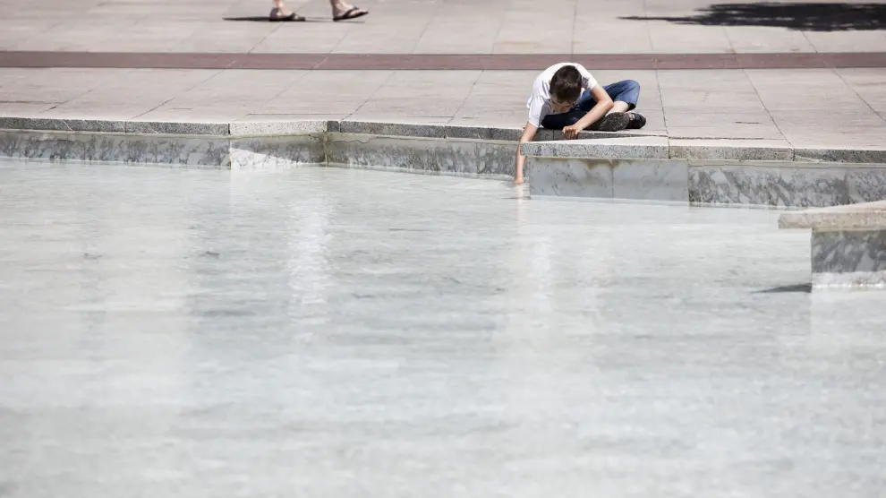 Un niño se refresca en una fuente en la plaza del Pilar.