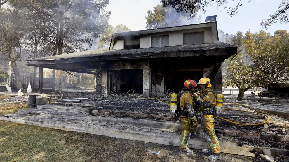 Dos bomberos conversan ante una de las viviendas afectadas por el incendio forestal en Llutxent (Valencia).