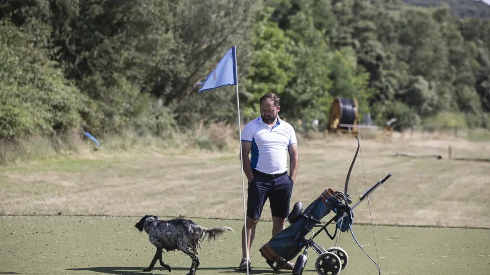 Jesús Alegre en el green del Hoyo 1 en su campo de 'ptch & putt' en Luesia, con un arco del tiro 3D contiguo y su perro guardián.
