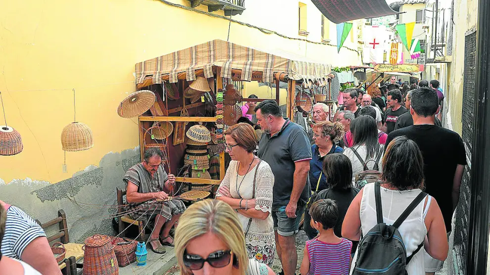 Un cestero muestra su oficio ante la mirada de los viandantes que llenan las calles de Rubielos.