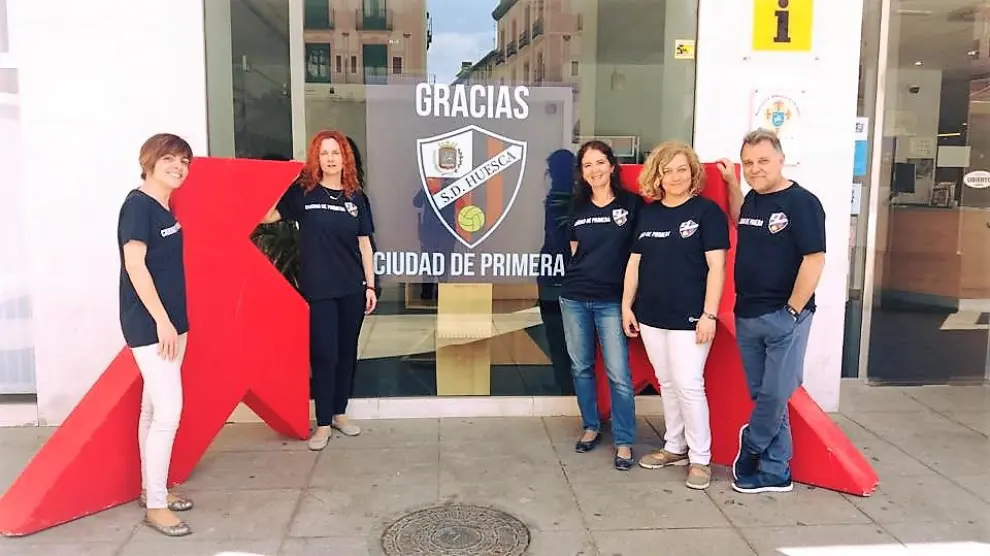 Los técnicos de Turismo delante de la oficina con el cartel que refleja el ascenso de la SD Huesca a Primera División
