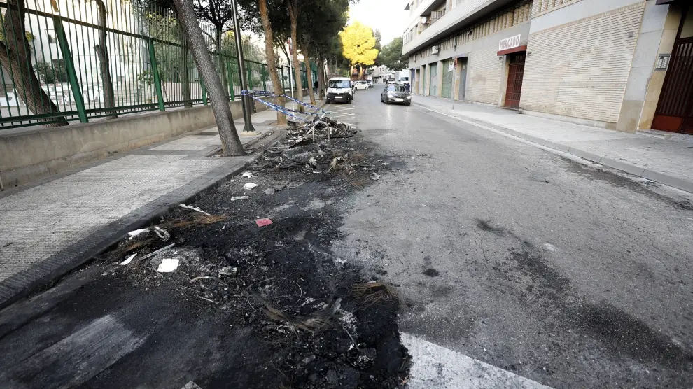 Restos del contenedor y el vehículo quemado en la calle de San Eugenio en Torrero.