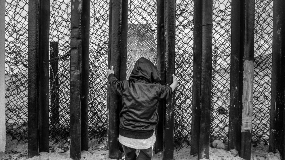 Un niño se agarra a los barrotes del muro fronterizo en la playa de Tijuana
