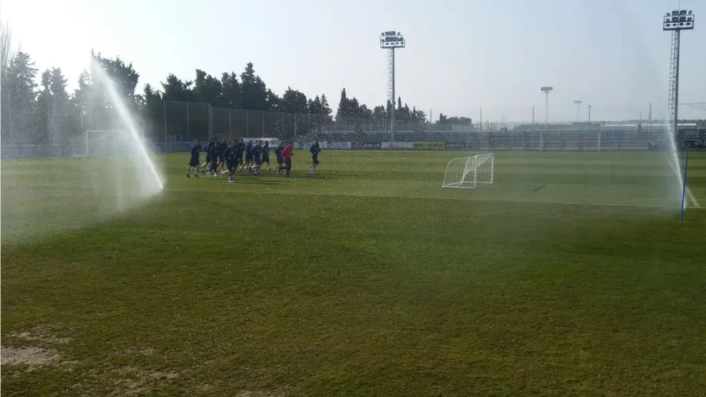 El grupo de jugadores del Real Zaragoza, al inicio del entrenamiento de este martes entre los aspersores de la Ciudad Deportiva.