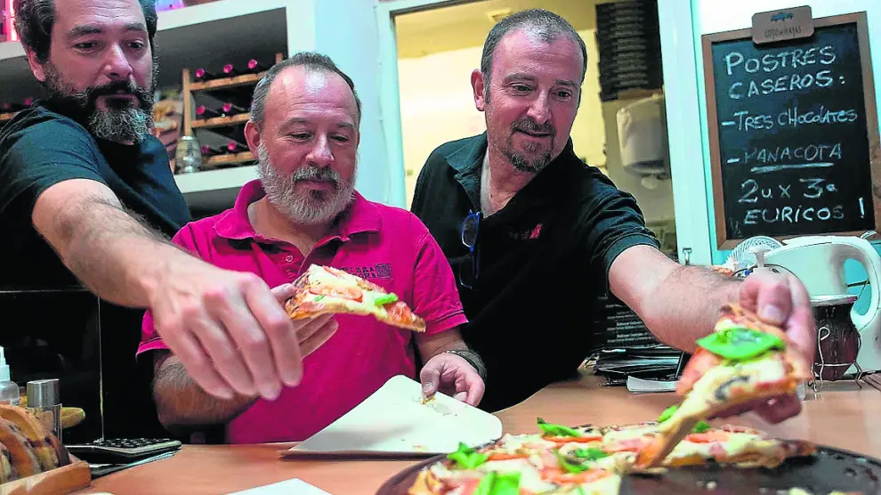 Hernán Romero, Javier Harguindeguy y Pablo Lozano cogiendo una pizza negra.