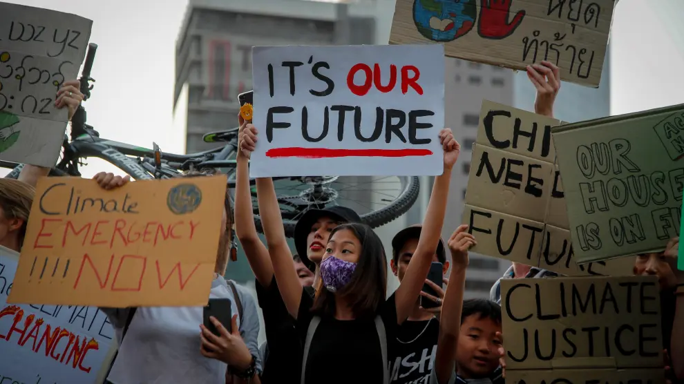Varias personas sostienen pancartas con mensajes como "Este es nuestro futuro" durante una manifestación contra la crisis climática, este viernes a las afueras de un parque en Bangkok