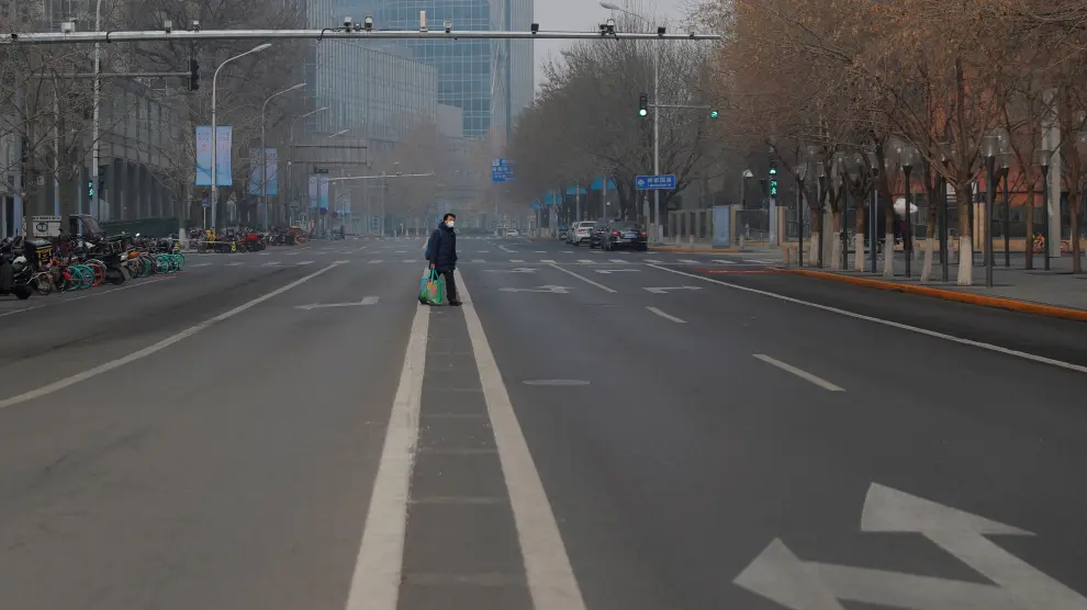 Un hombre con mascarilla camina por una calle desierta en Pekín
