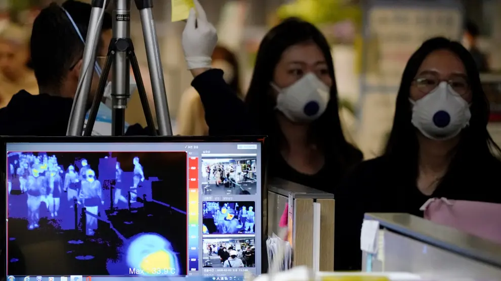 Pasajeros con máscaras pasan por una cámara térmica en el aeropuerto de Hong Kong