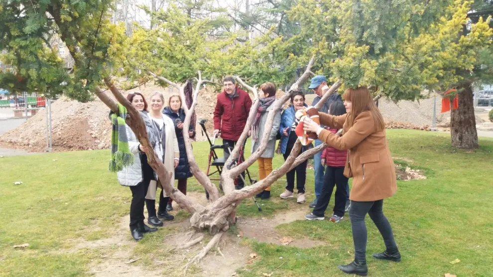 Miembros de la Asociación de Esclerosis Múltiple con la alcaldesa de Teruel cuelgan bufandas en árboles del Parque de los Fueros para quien las pueda necesitar.