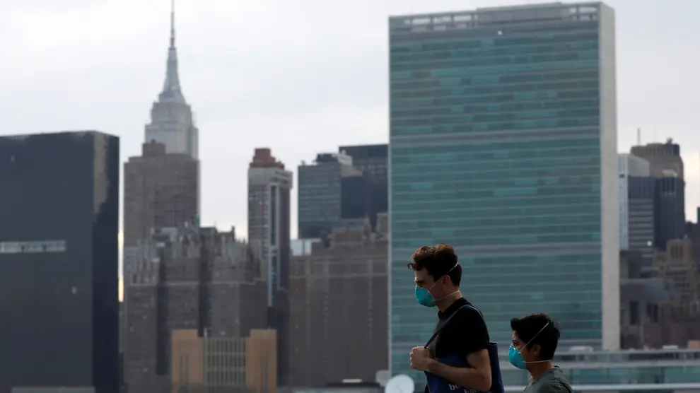 People in protective masks walk in front of the Manhattan skyline along the waterfront of Long Island City as the coronavirus disease (COVID-19) outbreak continues in the Queens borough of New York City