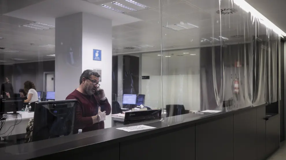 Un funcionario, atendiendo el teléfono detrás del mostrador del juzgado de guardia de Zaragoza, protegido con una cortina de plástico.