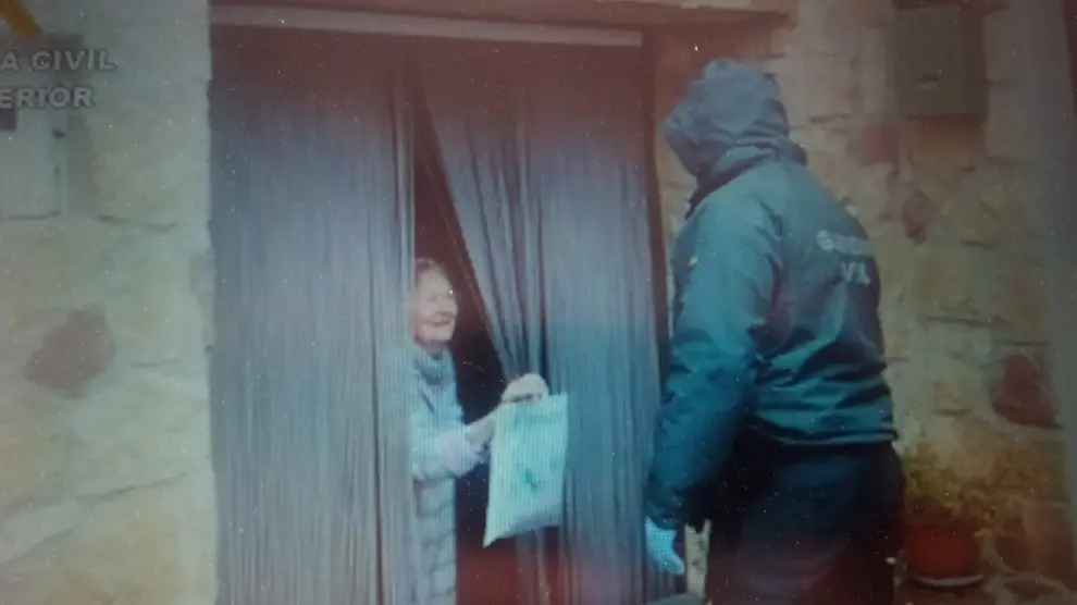 Un guardia entrega un paquete de medicinas a una pareja de mayores en un pueblo.