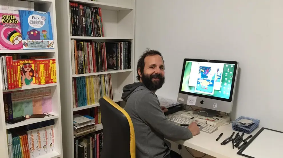 El ilustrador Artur Laperla, en su mesa de trabajo, junto a parte de su biblioteca.