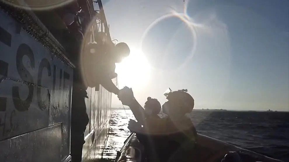 A still image taken from a video shows a rescuer of Spanish NGO Open Arms helping a migrant boarding a dinghy in the Mediterranean Sea