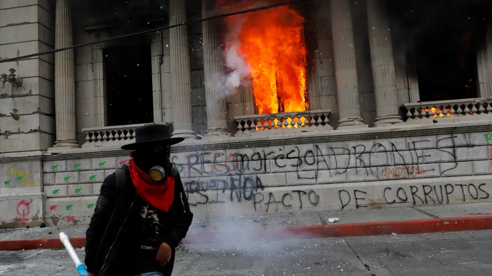 Un hombre que participaba en las protestas camina junto al Congreso guatemalteco en llamas.