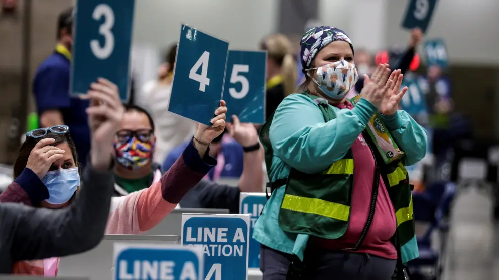 Vaccinator lead Delvalle wears a Dr. Fauci mask as volunteers clap while welcoming their first patients at a vaccination site at Lumen Field Event Center in Seattle