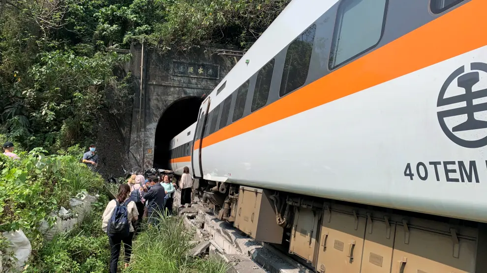People walk next to a train which derailed in a tunnel north of Hualien