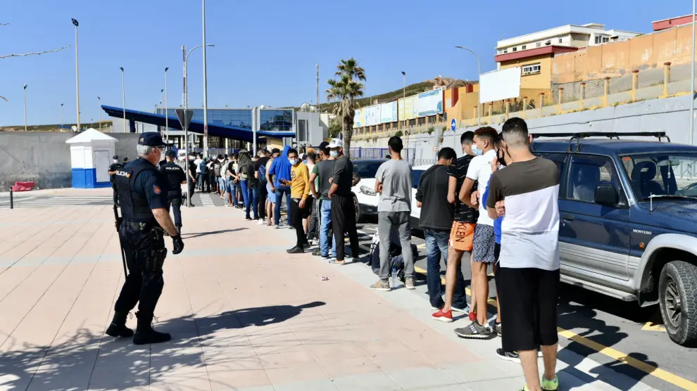 Varios migrantes procedentes de Marruecos hacen cola en las puertas de la frontera de Ceuta donde agentes de la Policía Nacional reparten citas para solicitud de asilo.