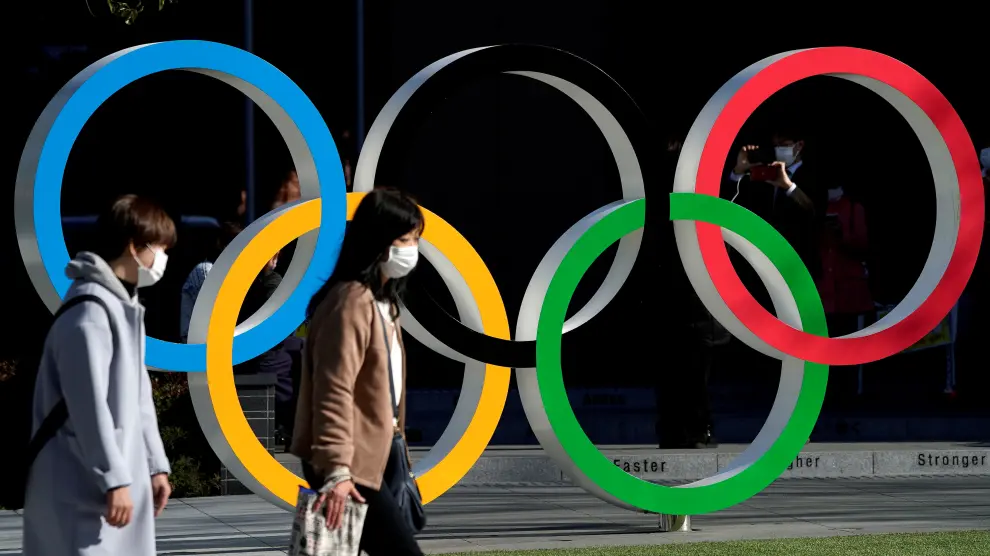 Una personas con mascarilla pasan por delante de los aros olímpicos en Tokio.