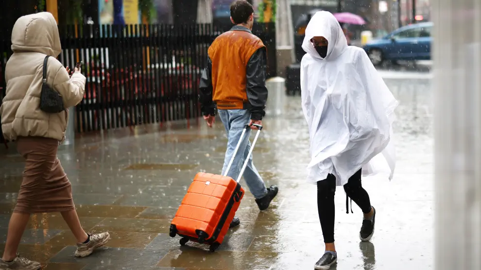 A person wearing a poncho and protective face mask walks through heavy rainfall, amid the coronavirus disease (COVID-19) outbreak, in London