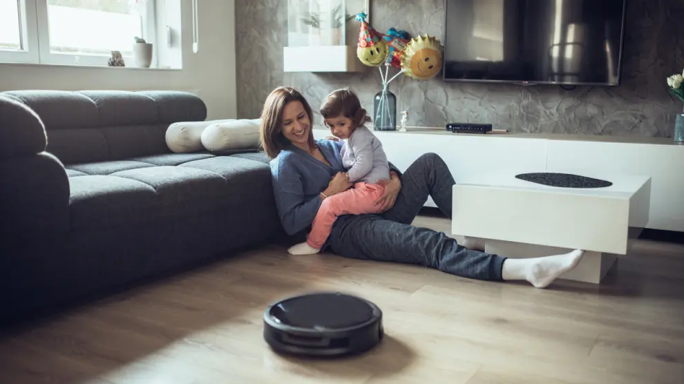 One woman, at home relaxing with her little daughter on the floor, while robot vacuum cleaner is working.